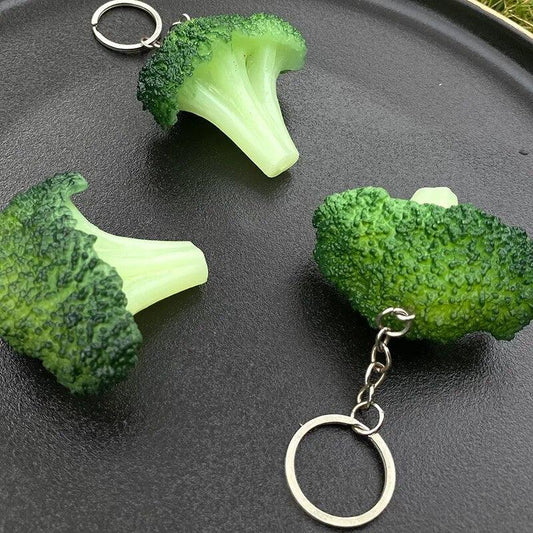Three Silly Sausage Broccoli Keychains on a black plate.